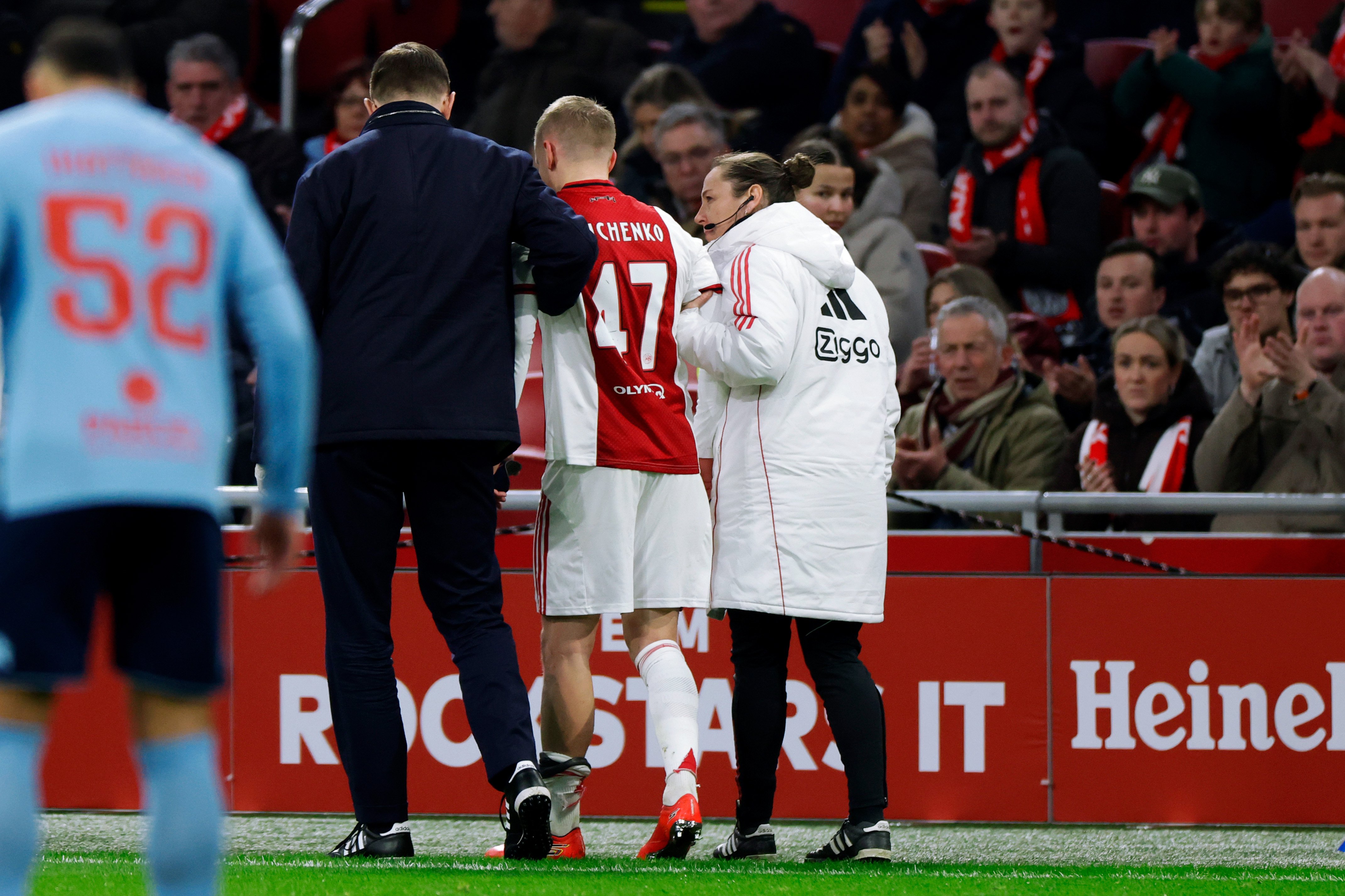 Oleksandr Zinchenko verlaat zichtbaar aangeslagen het veld van de Johan Cruijff ArenA, ondersteund door stafleden van Ajax na zijn vroege blessure.